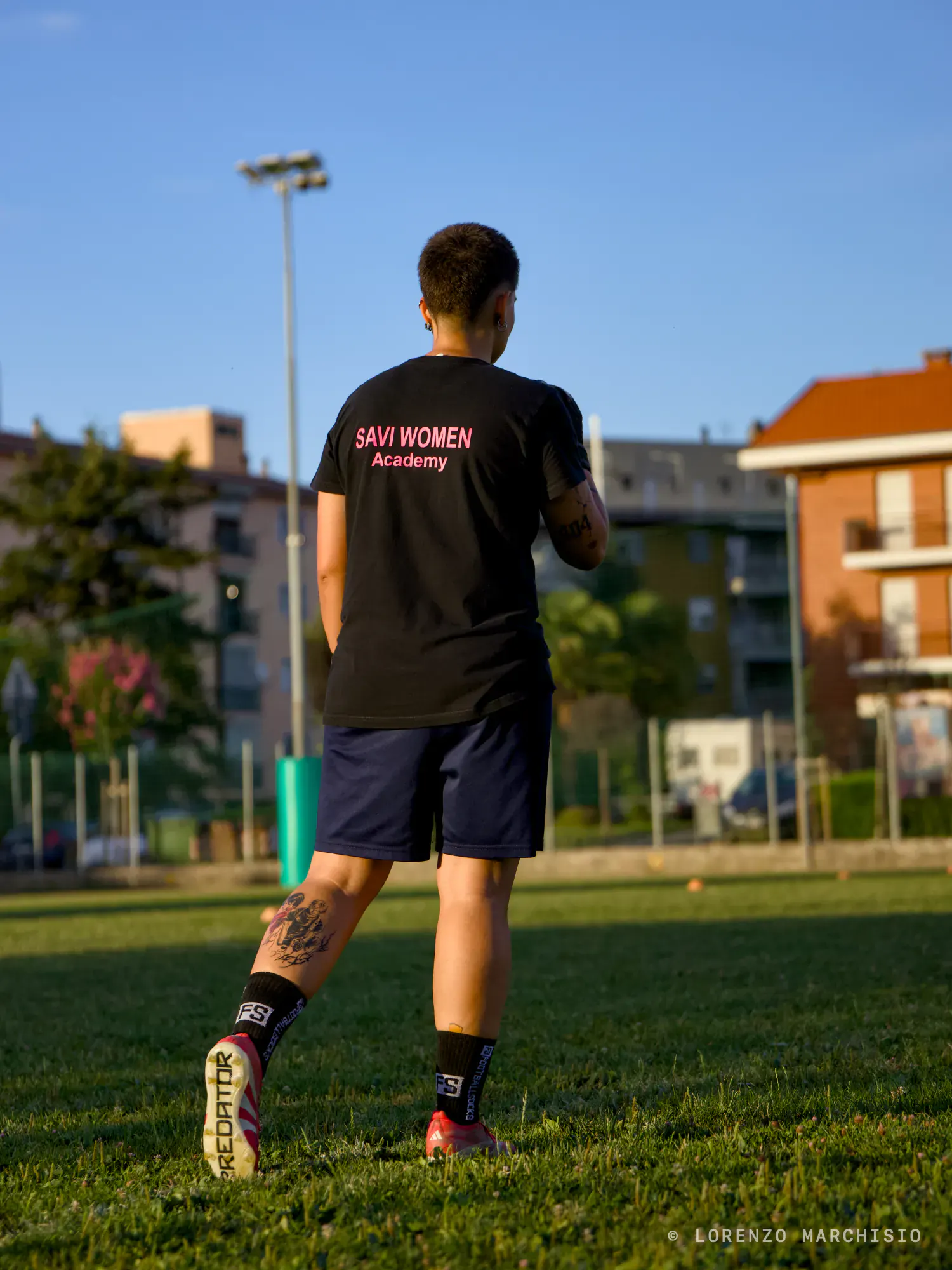 Footballer in a black shirt walking away across the pitch in evening light