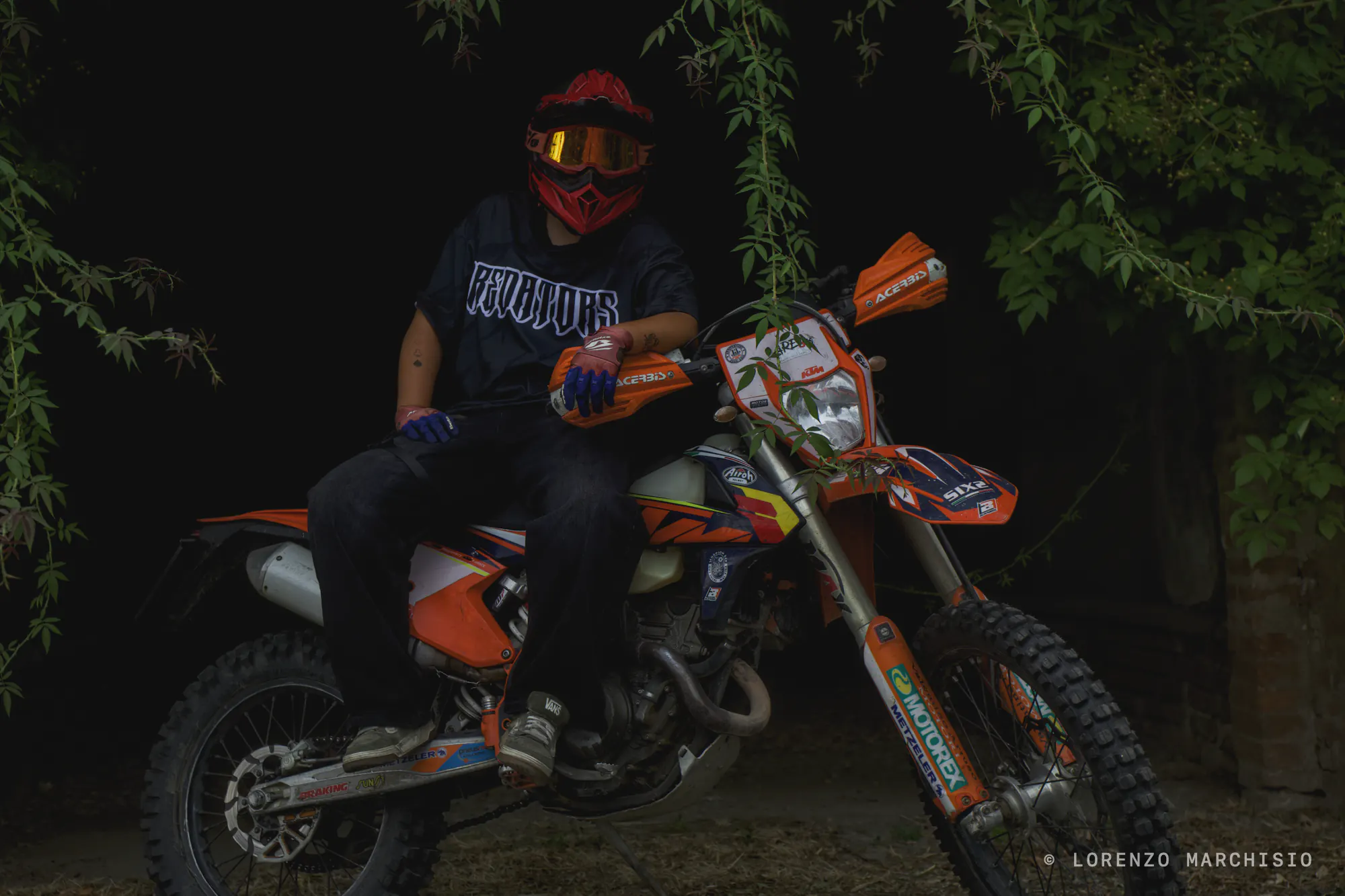 Rider in a red helmet astride an orange enduro bike in the dark